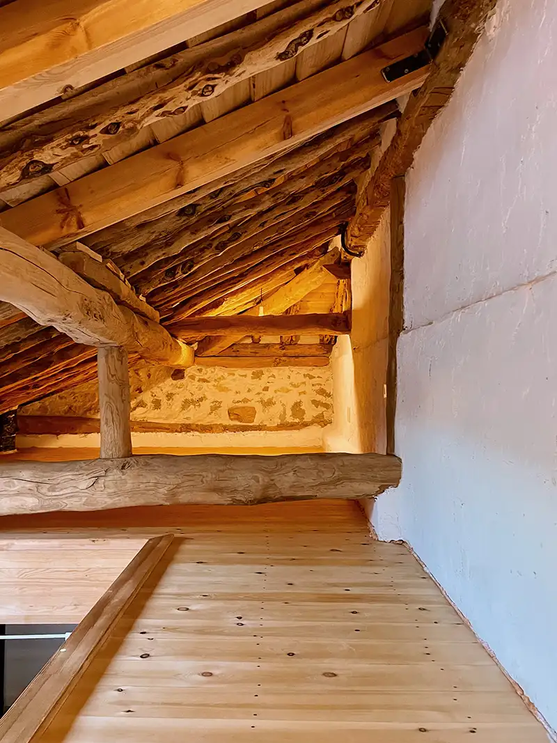 rehabilitacion-arquitecto-ignacio-barco-pedraza Detalle de un ático rehabilitado en Segovia, con vigas de madera rústicas y paredes de piedra expuesta.