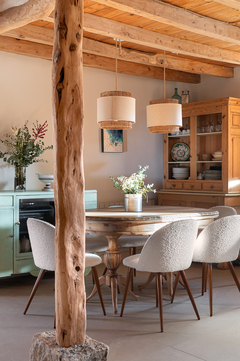 Casa de piedra de dos plantas con grandes ventanales, porche cubierto, zona de estar exterior y piscina en un jardín cerrado por un muro de piedra.